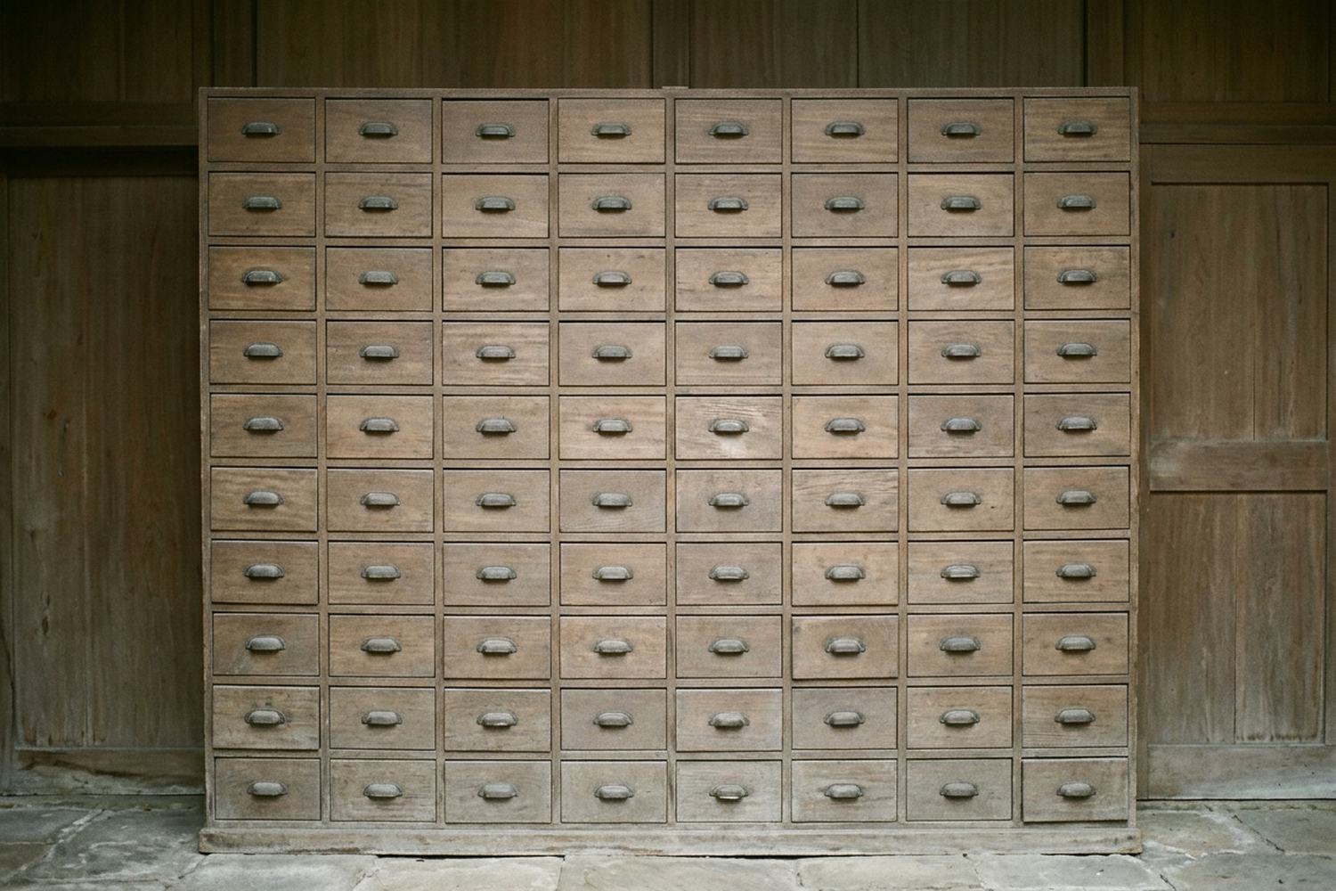 A tall wall of small wooden drawers filling the frame, every one shut and carrying a plain metal pull