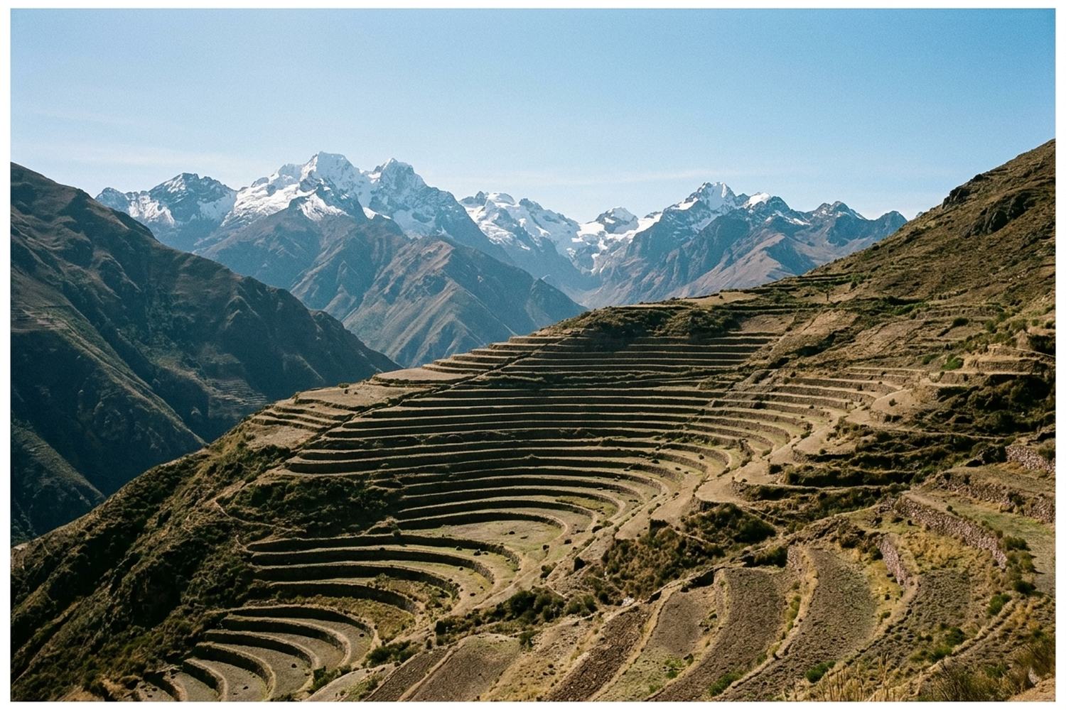Terraced slopes cut into a steep valley side with snow peaks standing behind